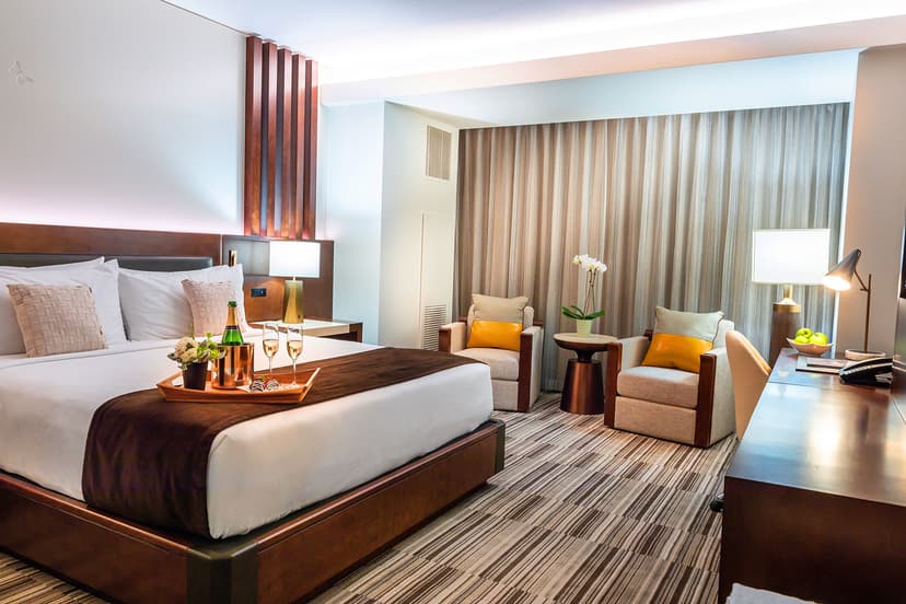 A pristinely made bed in the Monarch Suite with a warm glowing light and tan furniture