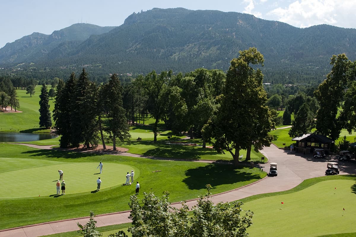 Several golfers stand around a putting green watching a player put their ball into a hole at The Broadmoor Golf Club in Colorado.