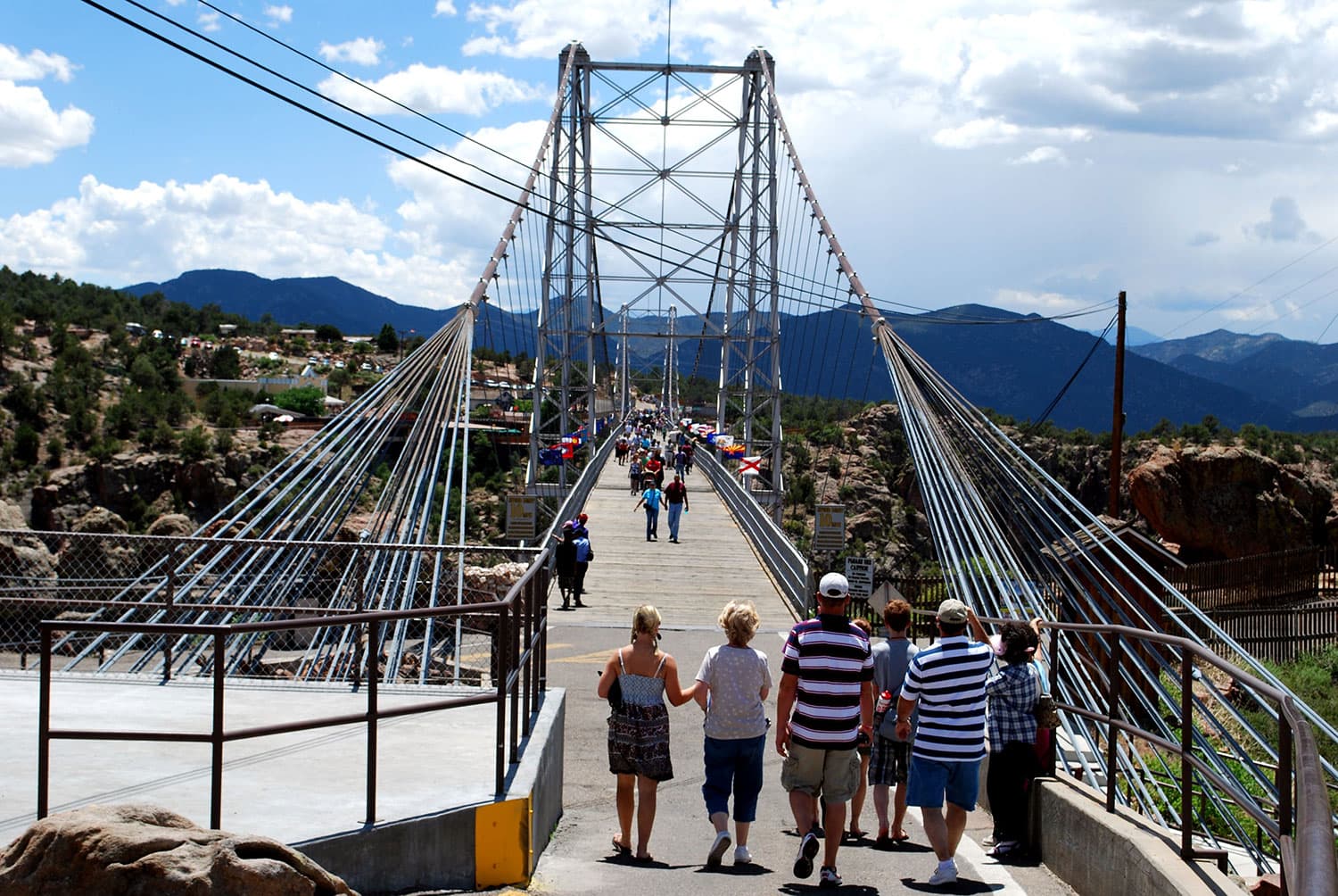A group of people walks towards the Royal Gorge Bridge in Colorado in an attempt to cross it. Other visitors trek across the bridge in the sunshine.