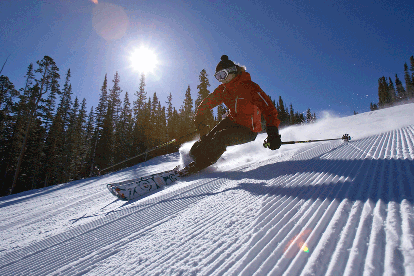 A skier carves a turn on a ski slope covered in corduroy — the tracks created by a recent grooming
