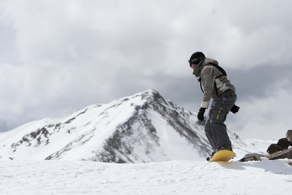 Snowboarder pausing on the edge of a snowy slope with a mountain backdrop at Copper Mountain, Colorado.