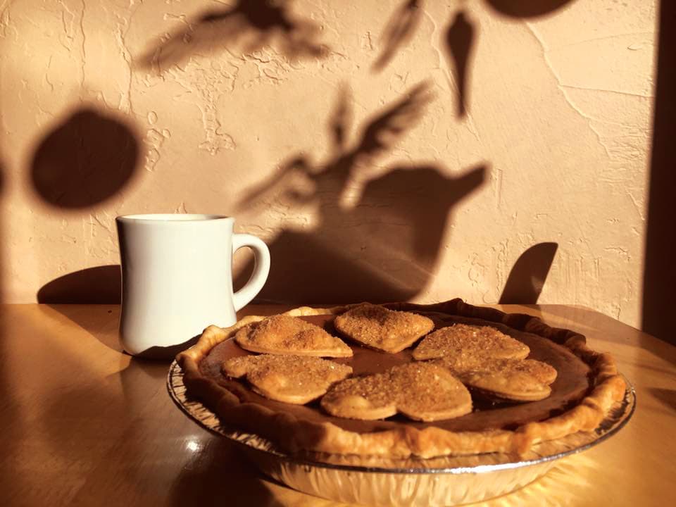 A white ceramic coffee mug sits on a table next two a freshly baked pie at the Pie Maker Bakery in Cortez, Colorado. Atop the pie are sugared heart-shaped crust pieces.