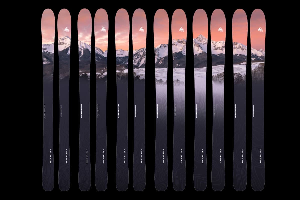 Customized skis from Wagner Skis, Mountain Village near Telluride, are set up in a line and together create a snowy mountain scene with a pink sunset.