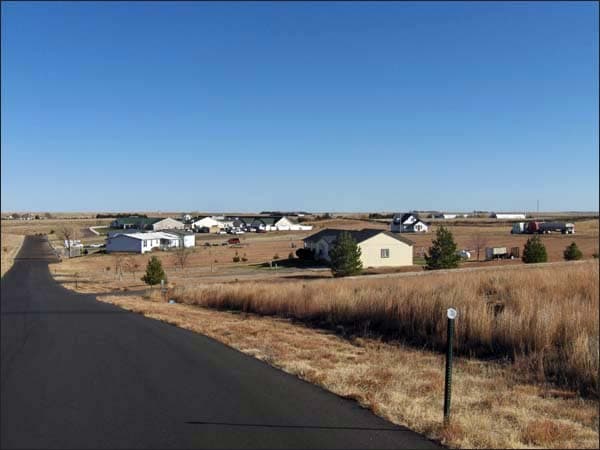 On a blue-sky day, houses sit amongst yellow grasses near a freshly paved road in Wray.