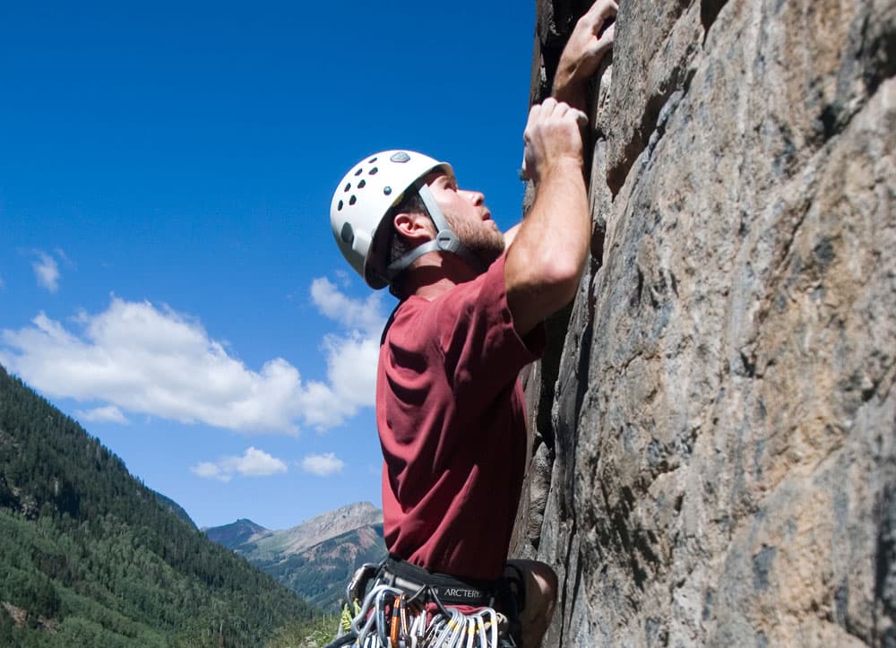 A man in gear climbs up the face of a giant rock