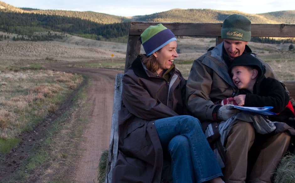Two adults and a child are dress in coats and knitted hats and are smiling together on a hay ride at a Colorado dude ranch.