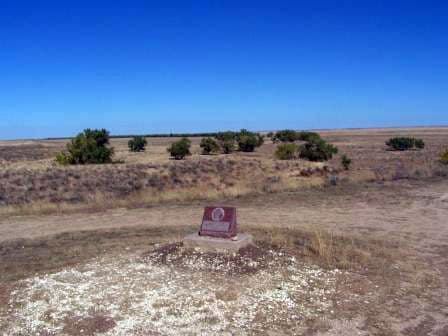 The historic site marker sits on the ground at Sand Creek Massacre National Historic Site. There's a bright-blue sky and brown grass. 