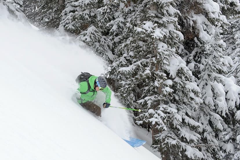 A person in a bright green winter jacket and gray helmet skis down a backcountry mountain in near Crested Butte, Colorado.