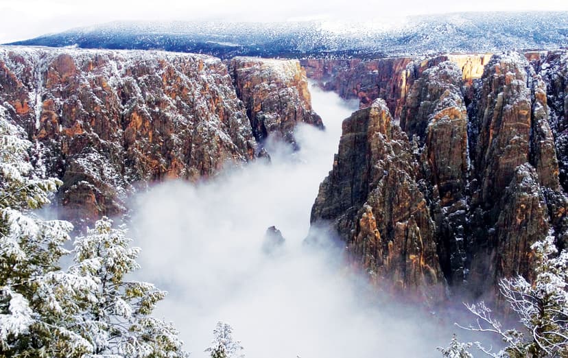A river of white fog hovers on the valley floor between the walls of Black Canyon