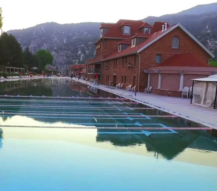 The mirrored, still waters of a hot springs pool with a red-brick lodge