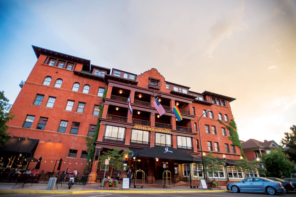 The red-bricked and multi-story Hotel Boulderado stands tall in Boulder, Colorado. Green ivy creeps up two sides of the hotel. Three flags fly from a balcony.
