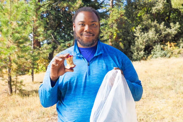 Hiking content creator, Nelson Holland holds an apple core and a trash bag. He is demonstrating that you need to throw away your eaten apple instead of throwing it on the ground while hiking