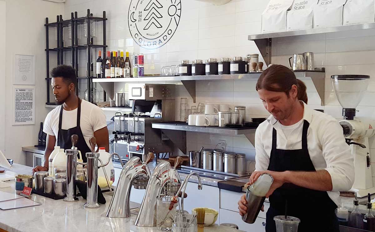Two people behind a coffee bar pour things and shake things