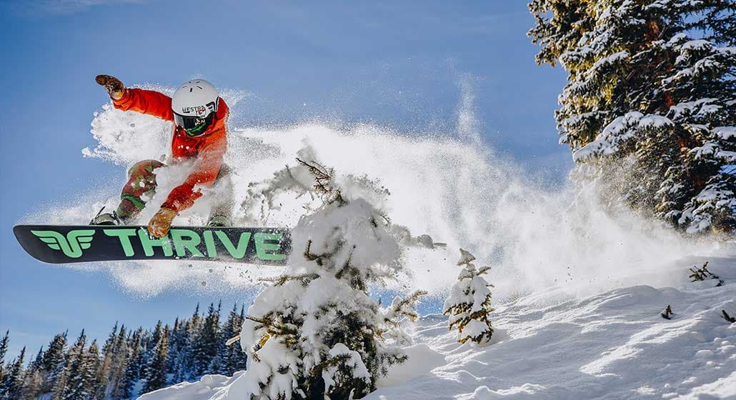 Snowboarder flying off a jump with snow trailing behind him