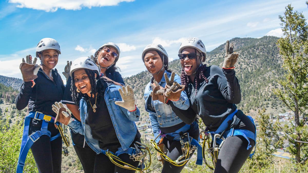Five friends smile and pose for the camera wearing protective gear before heading onto AVA Rafting & Zipline's Mountaintop Zipline course.