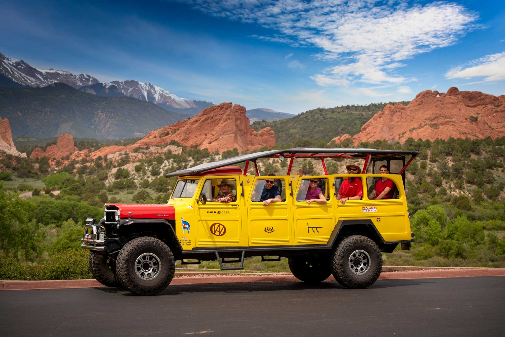 An extended yellow Hummer drives down the road with the red rocks of Garden of the Gods in the background