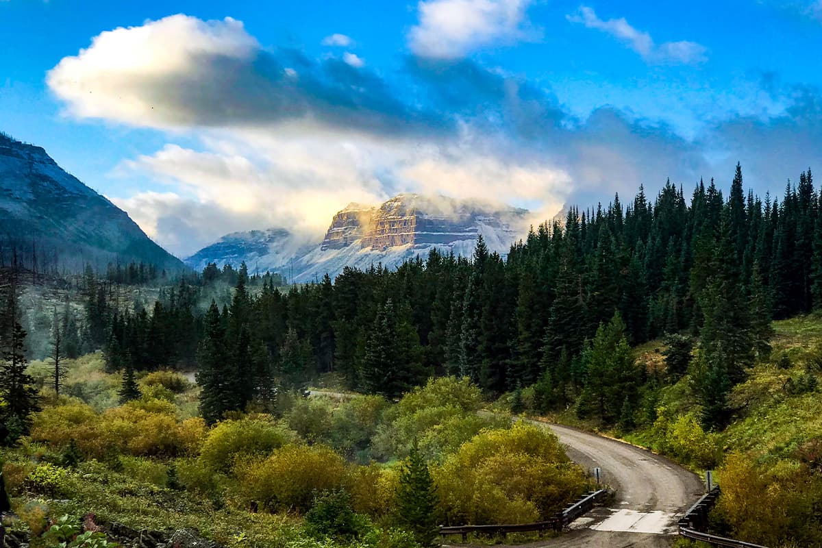 Snow-covered peaks are revealed from between clouds near Trappers Lake Lodge in Meeker. The surrounding landscape is lush with green pines and thick brush.