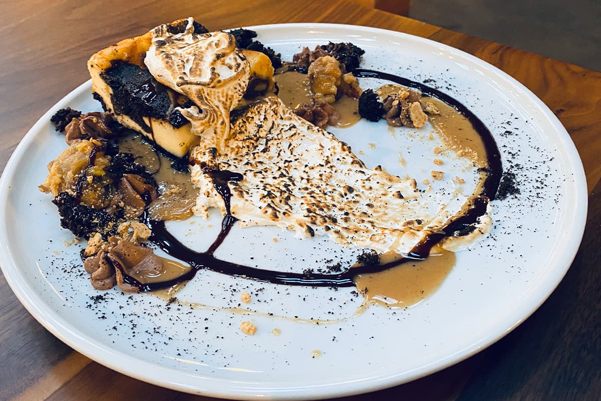 A decadent brownie with a gooey, flame-charred marshmallow on top and decorative chocolate sauce sits on a plain, white plate at the Historic Cow Palace Inn in Lamar, Colorado.