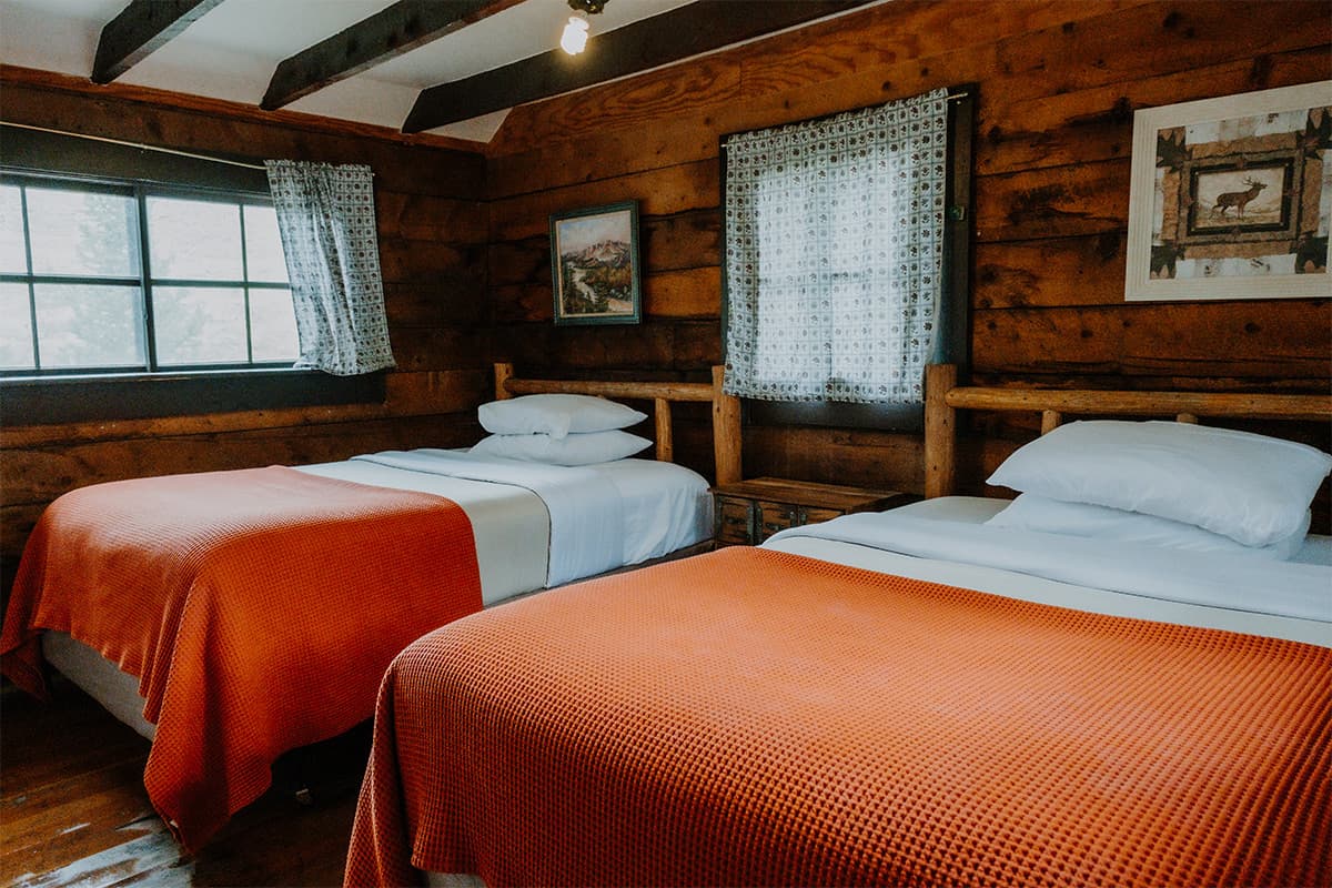 A cozy room at Trappers Lake Lodge features two ready-made beds with orange, waffle blankets and white pillows.