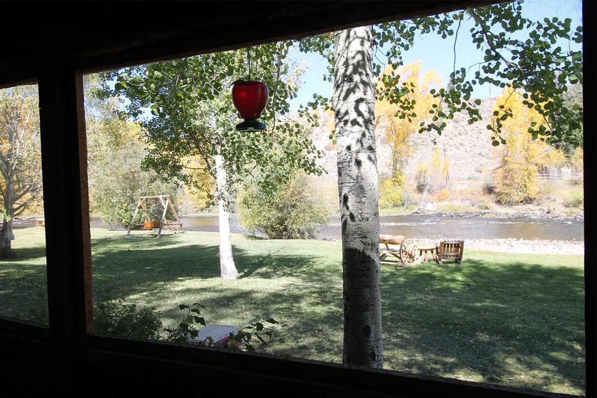 A private porch on a guest cabin at Bar Lazy J Guest Ranch in Colorado offers views of the rushing Colorado River and young, white-bark aspen trees.