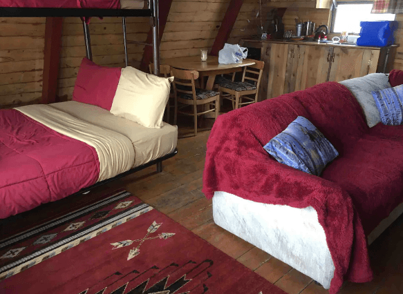 Interior image of Moose Haven Cabin with couch and bed covered in maroon-colored blankets