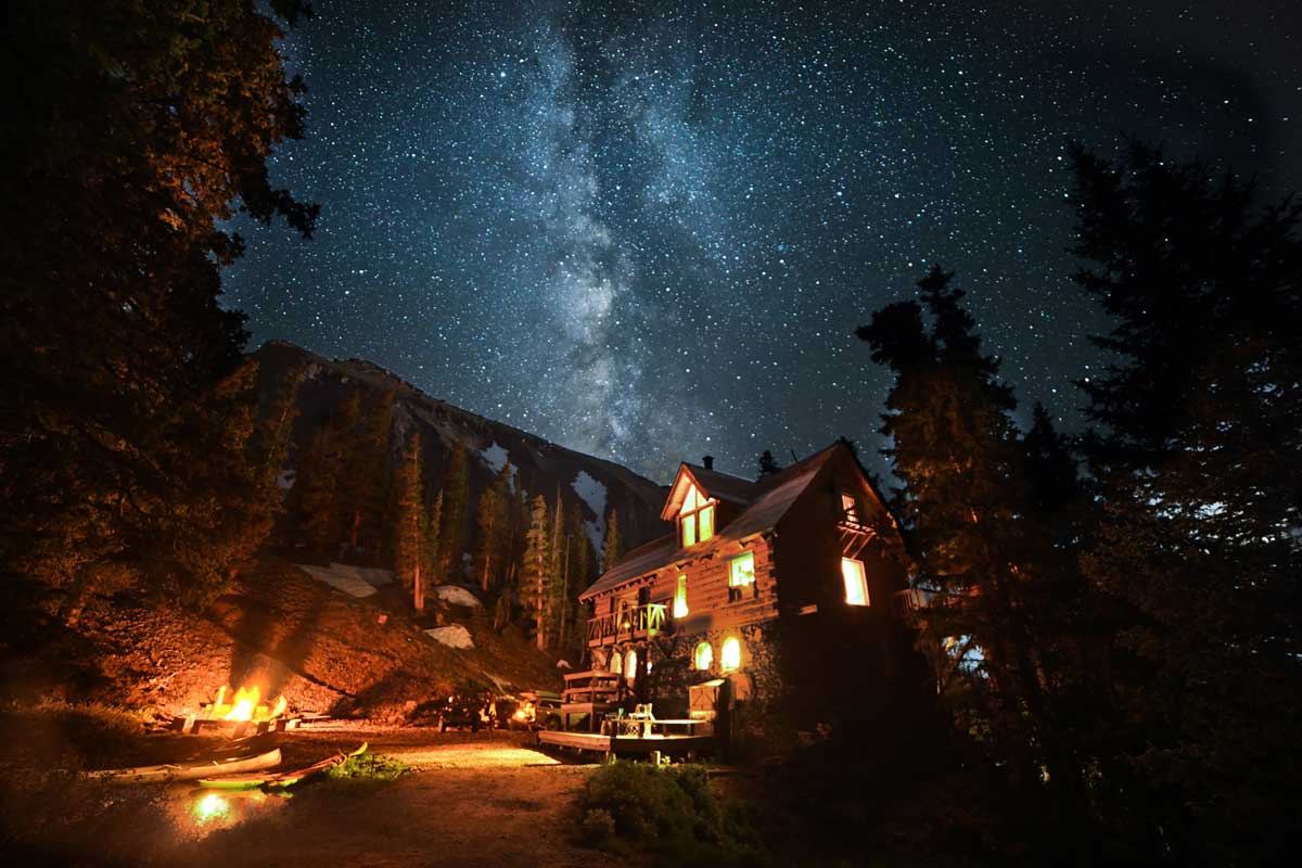 A starry night sky, a campfire and mountains and trees all around at The Observatory at Alta Lakes