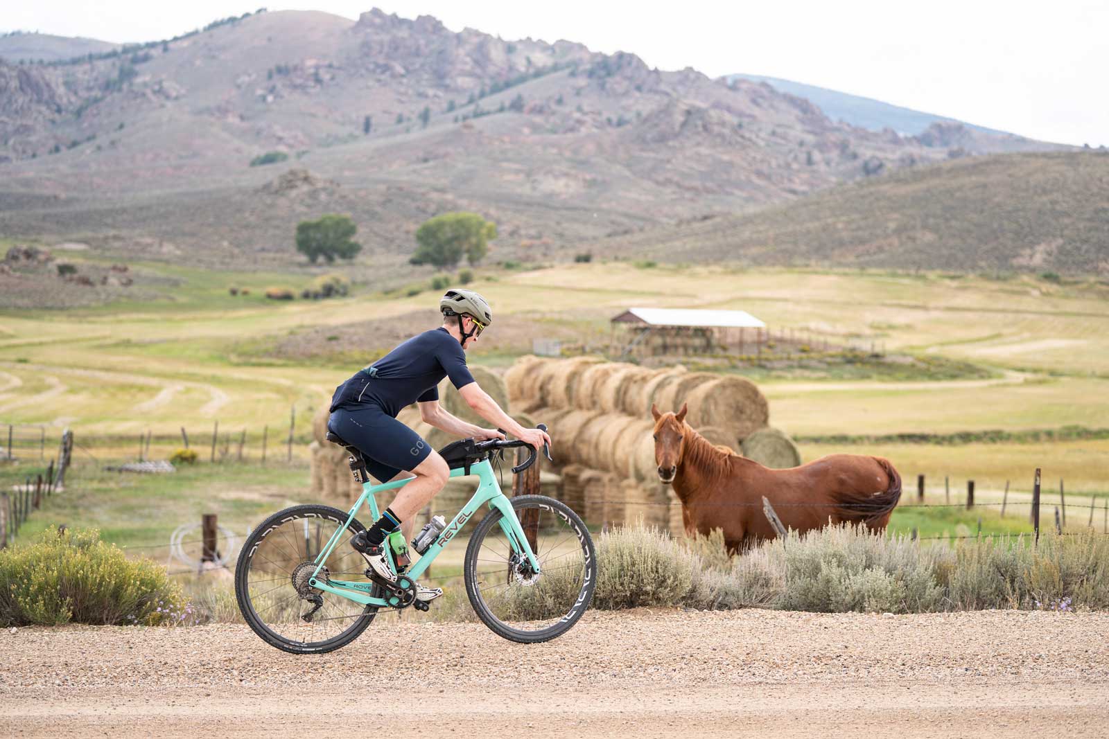 A gravel biker rides past a horse and stack of hay bales near Gunnison