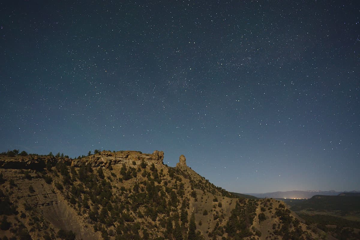 Night sky with stars above rock formations on a large hill