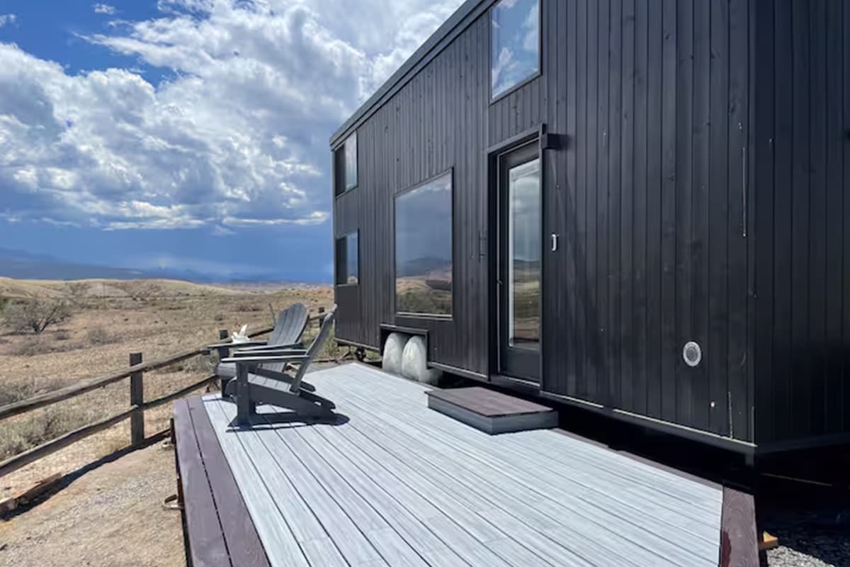 In Montrose, Colorado, two Adirondack-style chairs sit outside a small, black home on a porch.