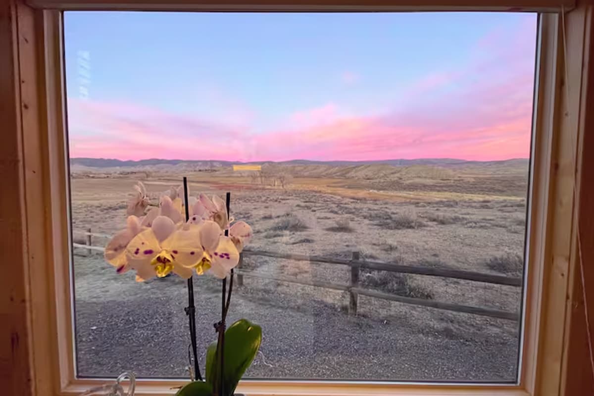 A tie-dye sunset of pink, purple and blue paints the sky outside a window of a tiny home in Montrose, Colorado.