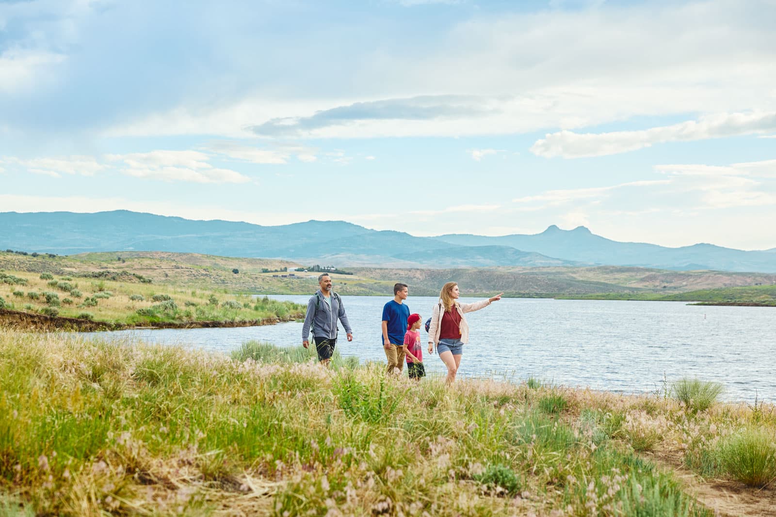 A family walks near a lake through green shrubbery