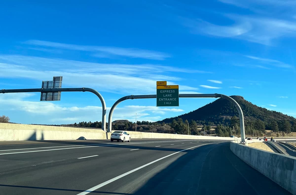 A white car driving smoothly along the Colorado Express Lane, featuring a mountain in the background.