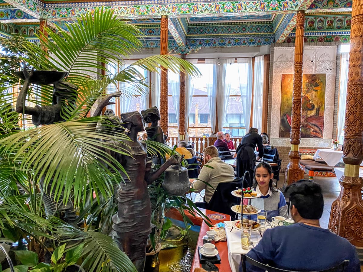 An interior shot of people dining at Boulder Dushanbe Teahouse surrounded by tropical plants, pillars with ornate carving and colorful mosaiced tiles
