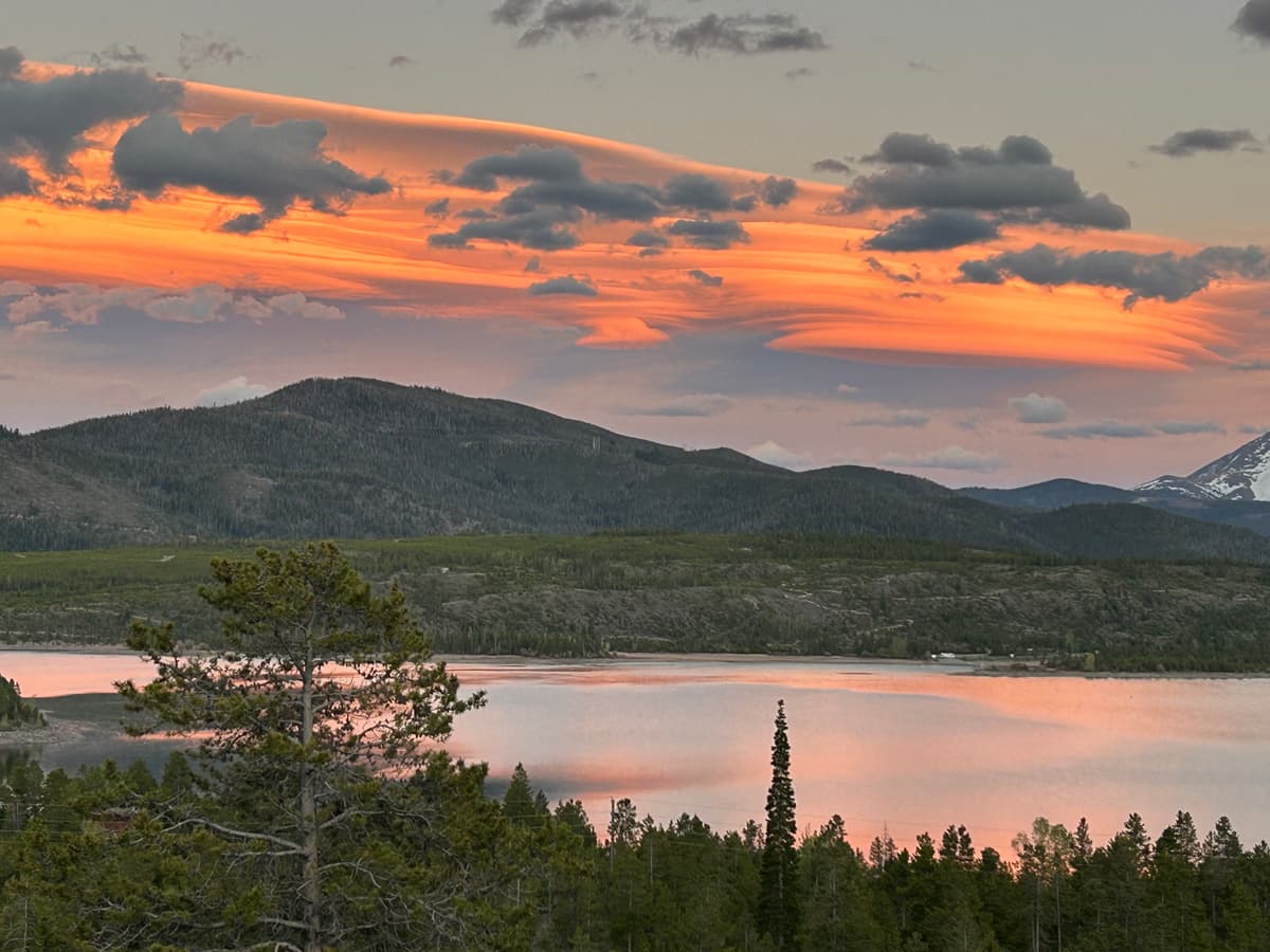 Lake Dillon in Colorado at sunset; the clouds and surface of the water are tinged rosy pink and mountains rise in the background.