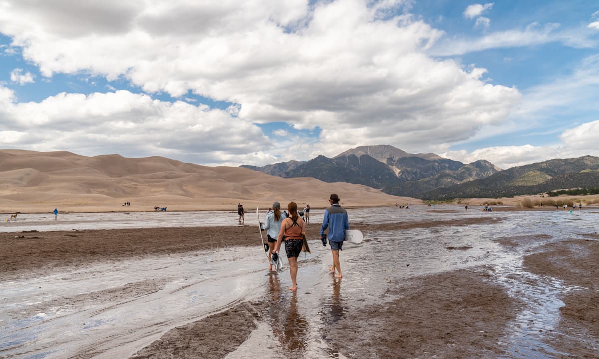 People walk through the shallow waters of Medano Creek, a seasonal snowmelt creek at Great Sand Dunes National Park and Preserve in Alamosa, Colorado