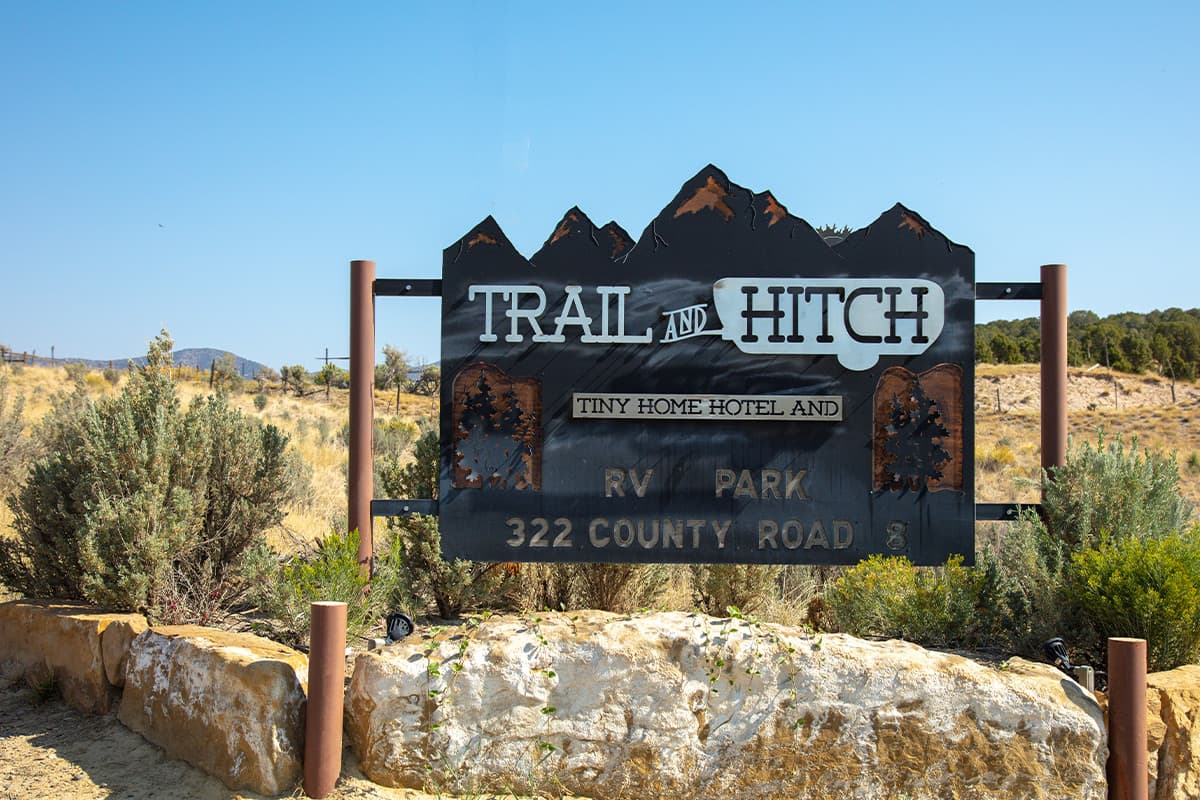 A custom metal sign with tree and mountain accents says, "Trail and Hitch Tiny Home Hotel and RV Park" near Meeker, Colorado.