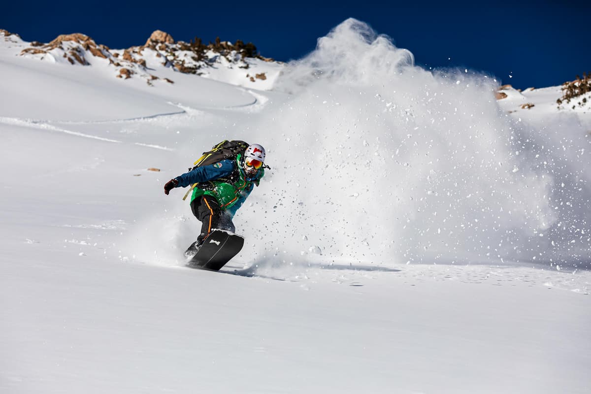 A person rides a splitboard through untracked snow leaving a trail of powder in their wake on a guided backcountry ski trip with Colorado Adventure Gudies.