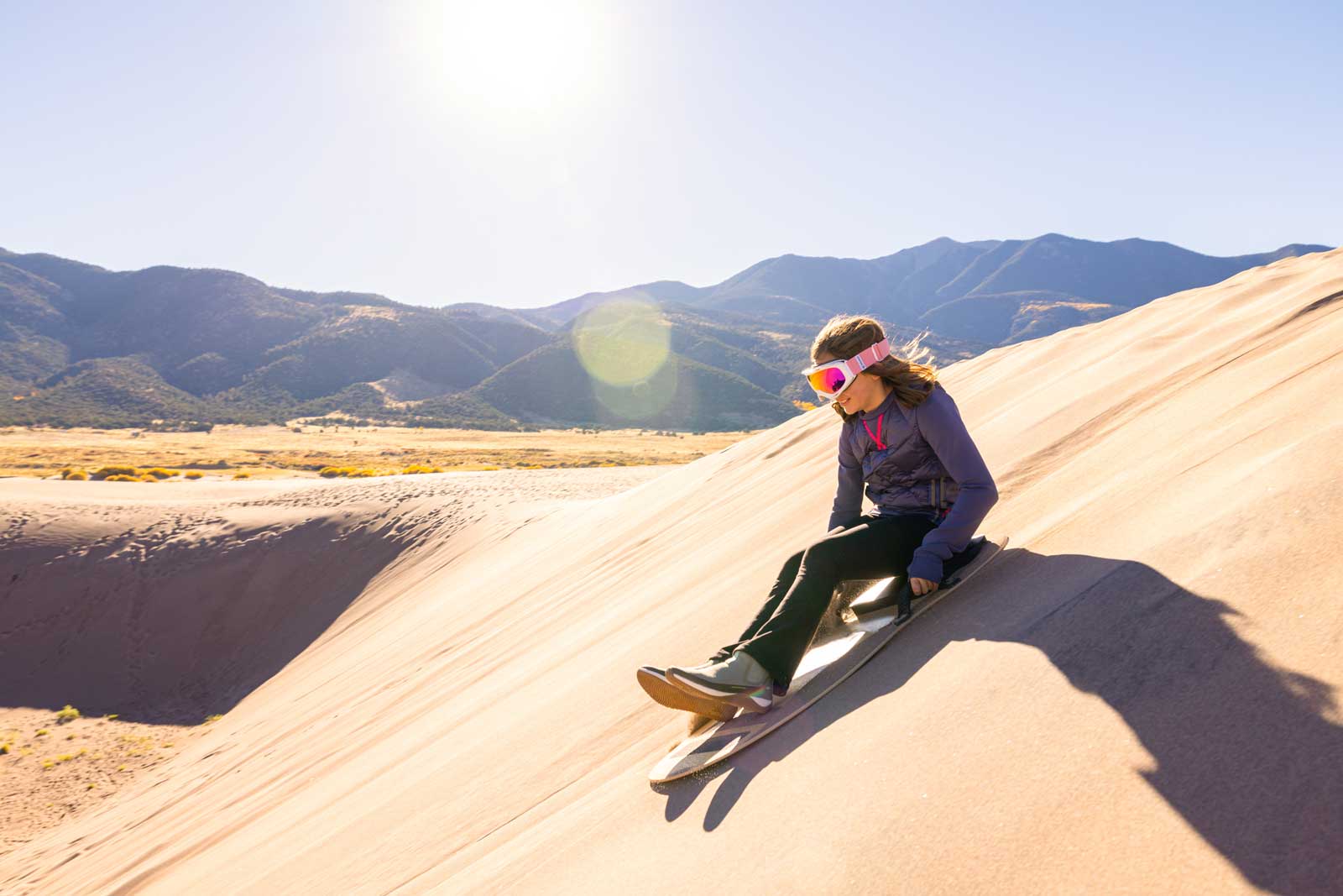 A teen sleds down a massive sand dune in Great Sand Dunes National Park