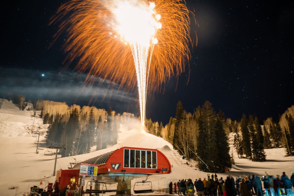 Fireworks lighting up the night sky with skiers and guests gathered below.
