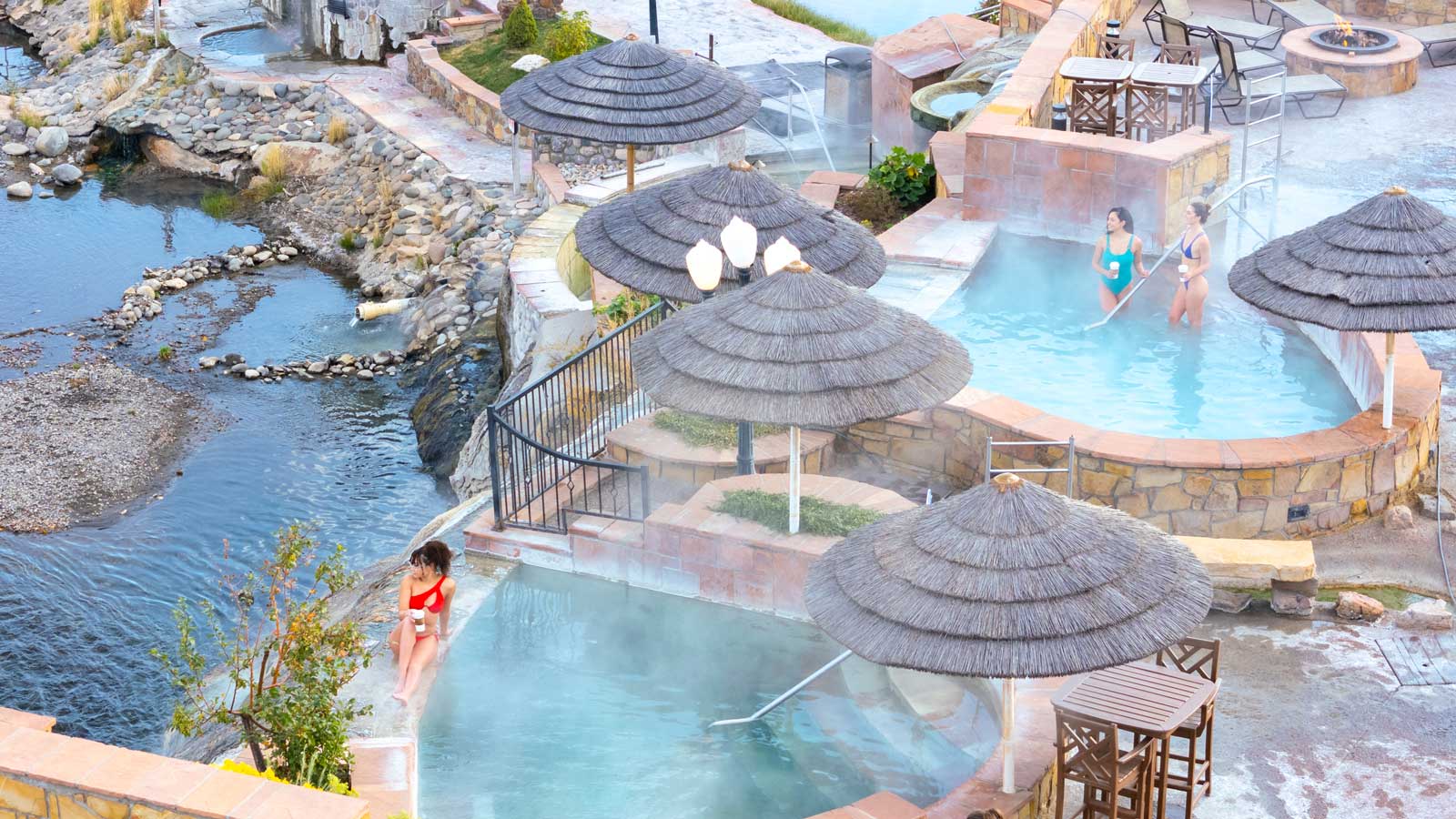 Three people sit around steaming hot-springs pools