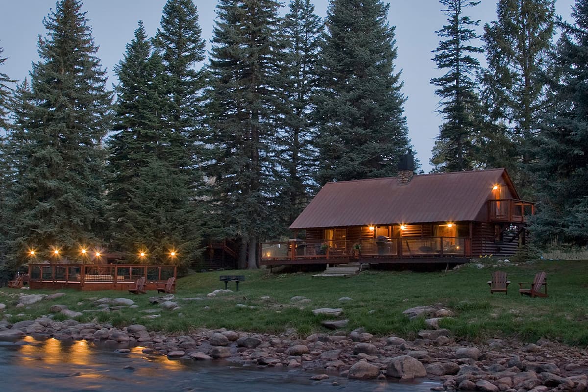 Evening falls and a riverside cabin at O-Bar-O Cabins, near Durango, CO, is lit with warm lights.