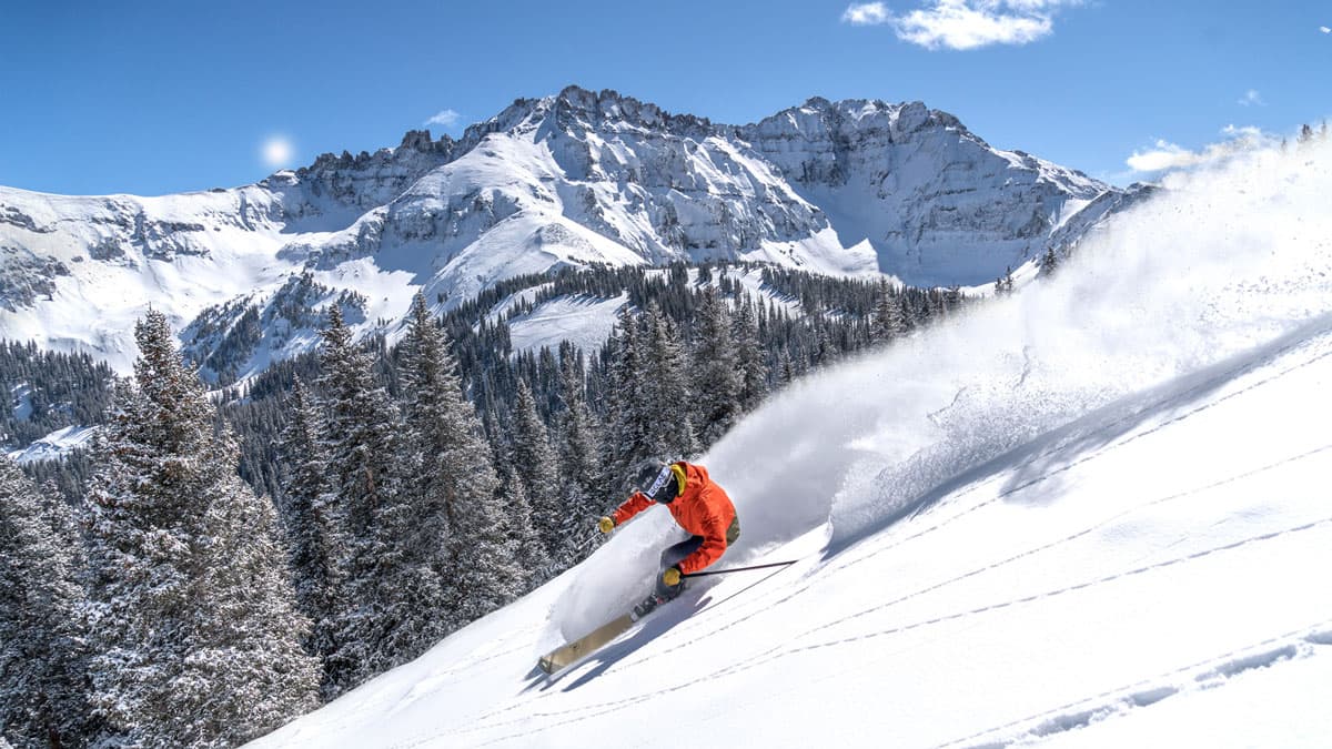 Person wearing bright orange jacket downhill skiing at Telluride Mountain Village in Colorado.