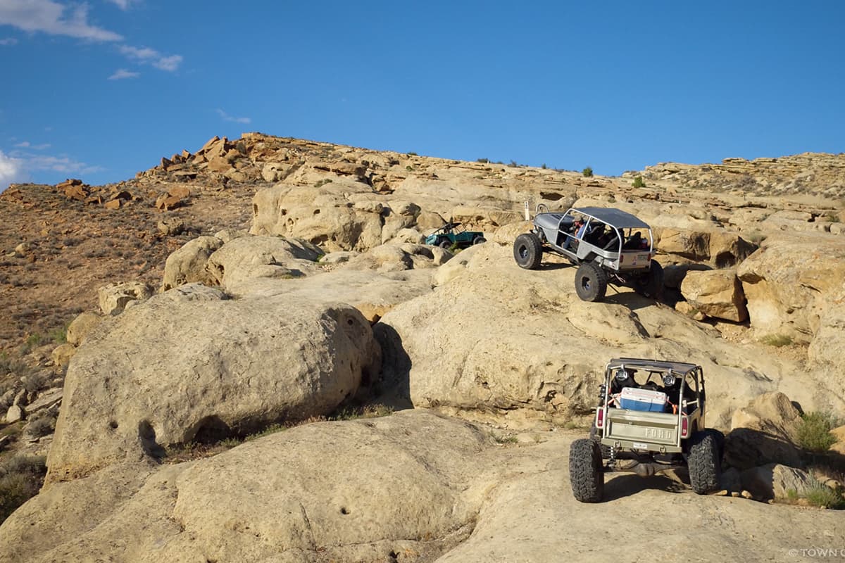 Two rock crawlers crawl over tan boulders in a park.