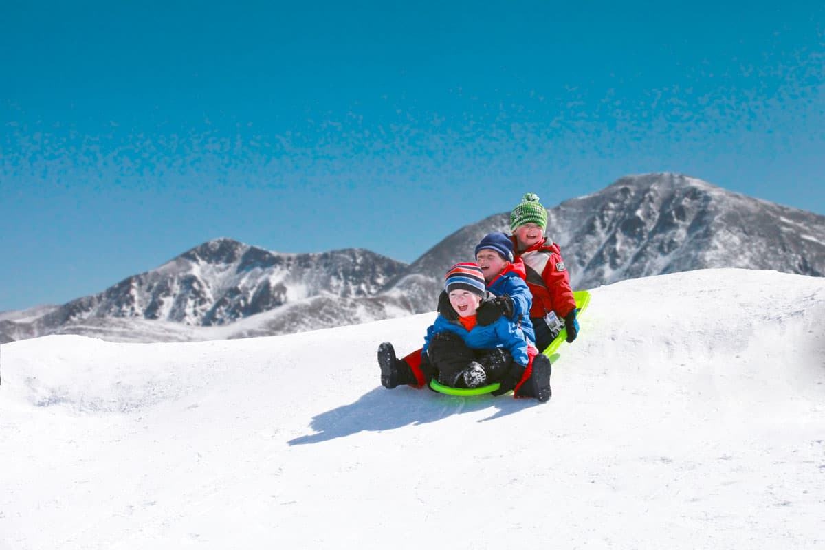 A group laughing on a sled racing down a snowly slope