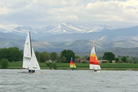 Three sailboats sit on Boyd Lake beneath the snow-capped Front Range mountains.