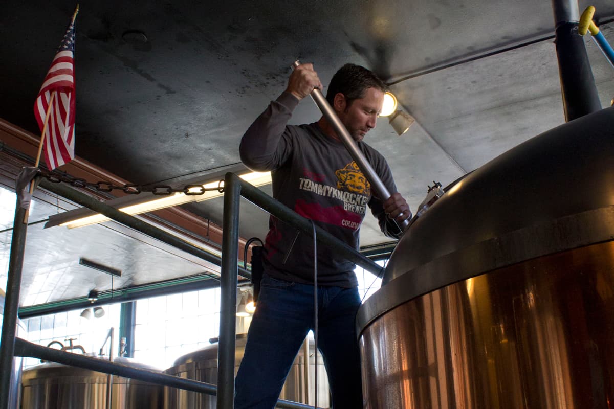 A person stirs a beer brew in a massive vat at Tommyknocker Brewery & Pub in Idaho Springs