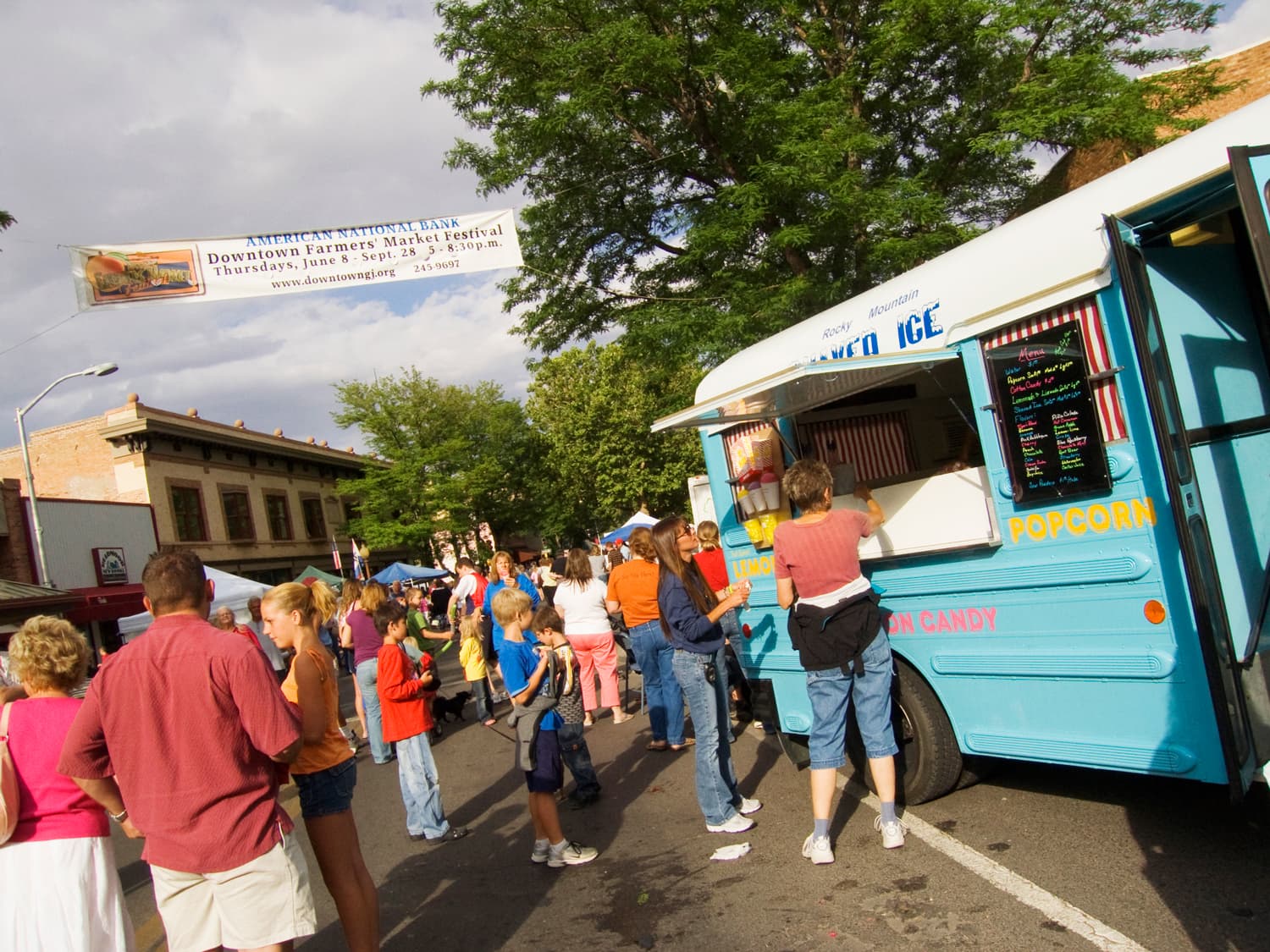 People line up at a blue food truck at weekly summer farmers' market in downtown Grand Junction