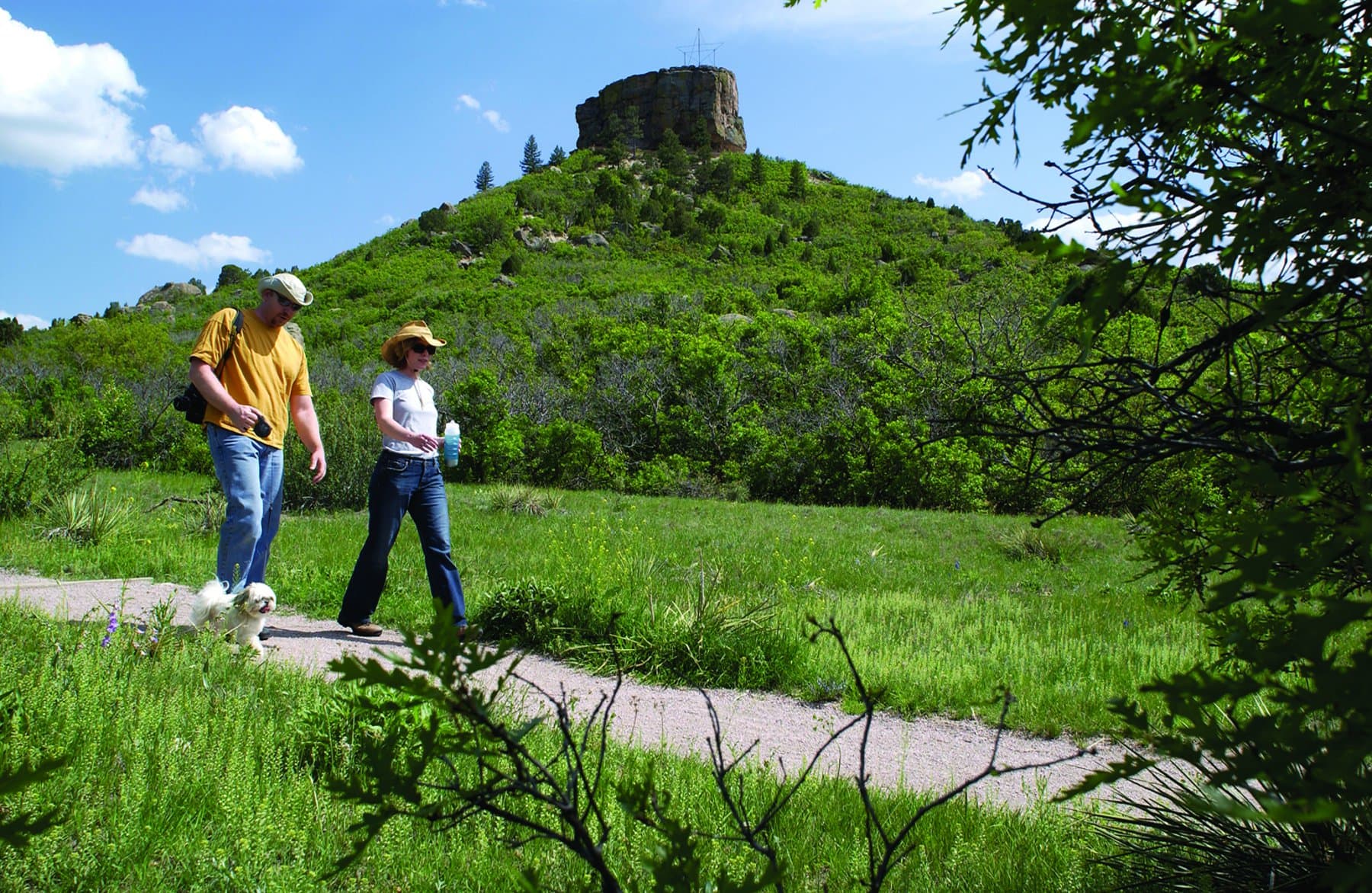 Two people walk along a flat trail beneath the shadow of Castle Rock
