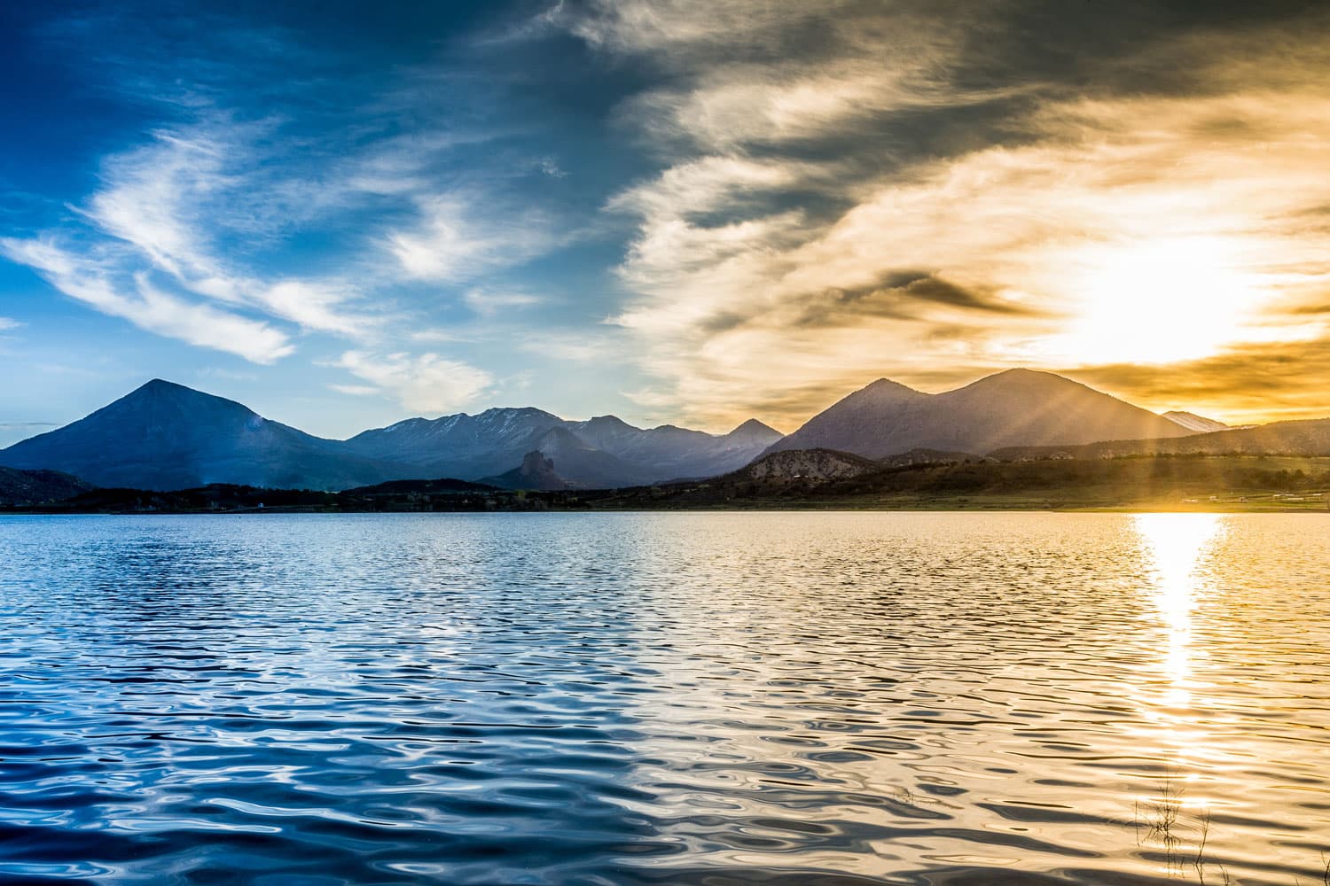 The sun is setting over the Blue Mesa Reservoir with half the image bathed in the golden light of the sun and the other in a blue-hue.