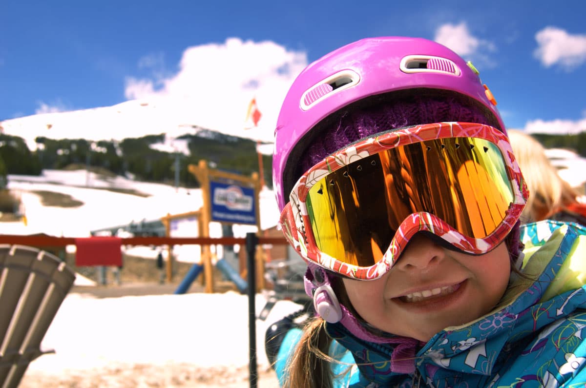 A smiling kid has a pink helmet and pink reflective snow goggles at Breckenridge Ski Resort.